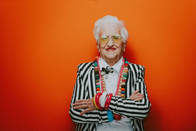 Portrait of stylish senior woman wearing colorful jewelry standing against red background