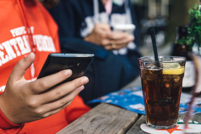 Midsection of woman text messaging on phone while sitting at table