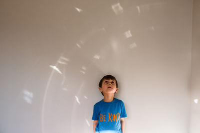 Boy wearing "be kind" shirt looking up at light pattern on wall