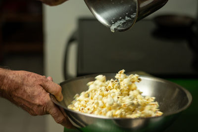 A male hand pours butter on popcorn and shakes the bowl to evenly distribute it.