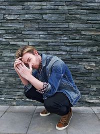 Portrait of young man crouching against wall