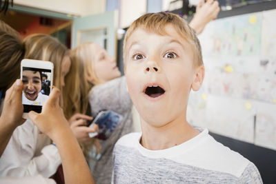 Surprised boy standing amidst friends taking selfie in corridor