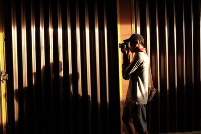 Side view of man photographing through camera while standing by shutter