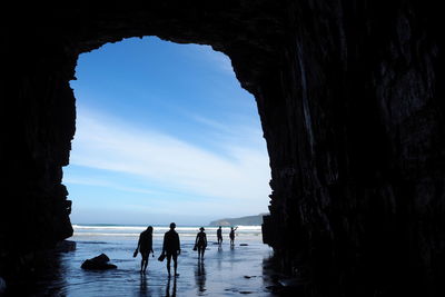 Silhouette people in cave at beach against sky