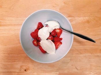 Directly above view of strawberries and whipped cream with spoon in bowl on table