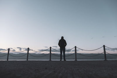 Rear view of silhouette man standing on beach against clear sky