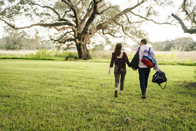 Rear view of couple holding hands while walking on grassy field at park