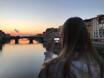 Reflection of woman photographing river in city