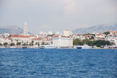 Sea by buildings in city against sky