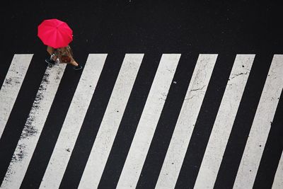 High angle view of woman with red umbrella walking over zebra crossing