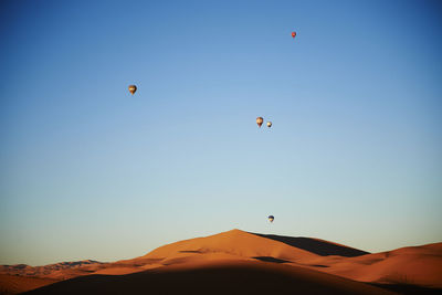 Hot air balloons flying in desert against clear blue sky