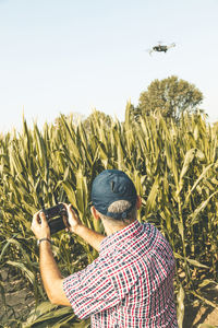 Man flying drone while standing amidst plants against clear sky