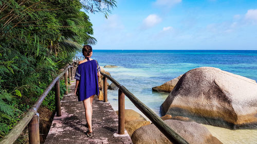 Woman in beach coverup walking on a wooden footpath over a sandy golden beach.