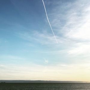 Vapor trail over sea against blue sky