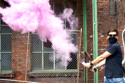 Portrait of man holding distress flare emitting pink smoke against windows