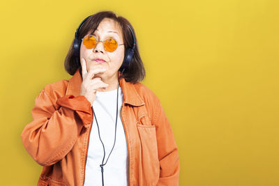 Woman with umbrella standing against yellow background