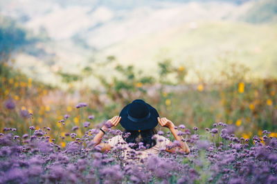 Rear view of woman wearing hat while standing amidst flowers