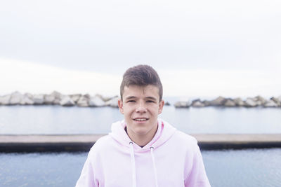 Portrait of smiling young man by lake against sky