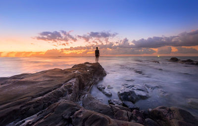 Full length of man standing on rock by sea against sky