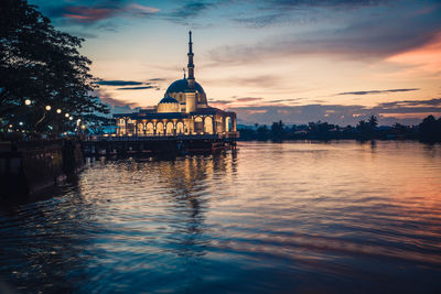 Building by river against sky during sunset