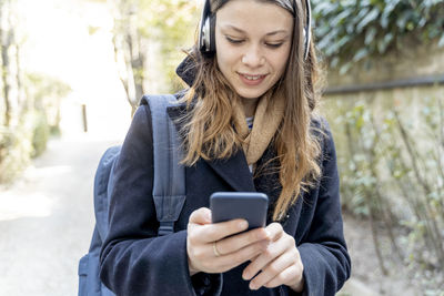 Young woman with headphones, using smartphone, walking in the city