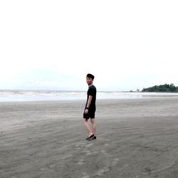 Full length of young man standing at beach against sky