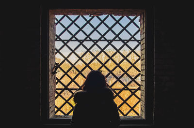 Rear view of silhouette woman looking through window in building