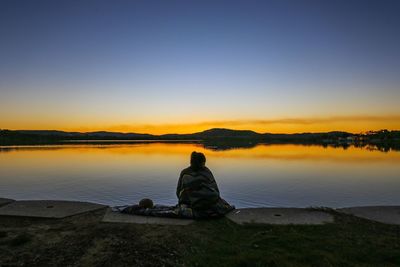 Rear view of women sitting against lake during sunset