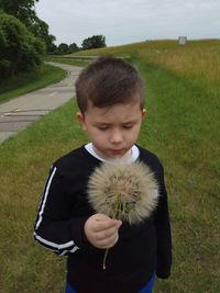 Boy holding dandelion while standing on grassy field