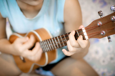 Midsection of woman playing ukulele while sitting on bed