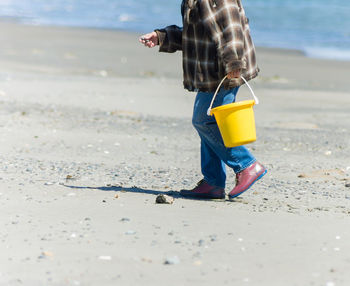 Low section of man with yellow bucket walking on beach