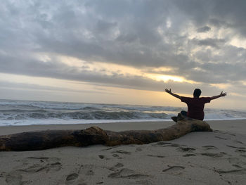 Rear view of man on rock at beach against sky