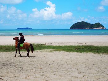 Man riding horse on beach against sky