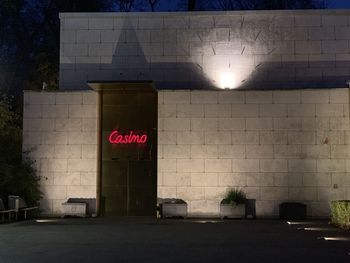 Information sign on wall by illuminated building in city at night