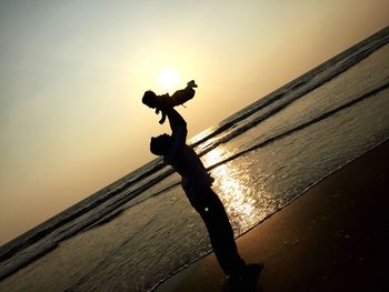 Silhouette man carrying child on beach