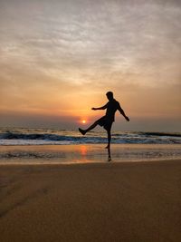 Silhouette man jumping at beach against sky during sunset