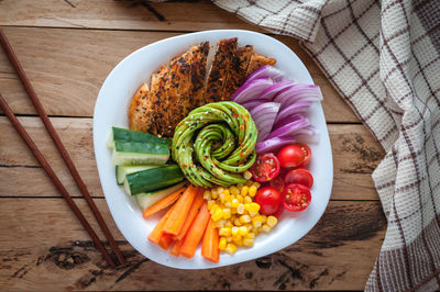 Buddha bowl with roasted chicken and fresh vegetables on wooden background, top view