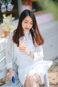 Woman drinking juice while sitting on bench