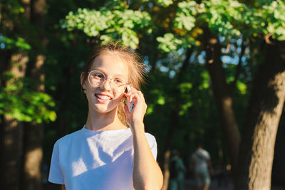 A girl in glasses happily talks on a push-button telephone among the trees