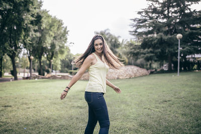 Full length portrait of smiling young woman standing on grass