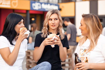 Young woman holding ice cream while sitting on outdoors