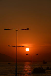 Silhouette street light by sea against sky during sunset