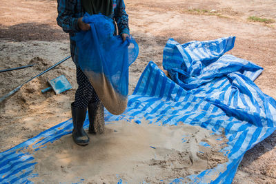 Low section of man holding sand in blue net at field