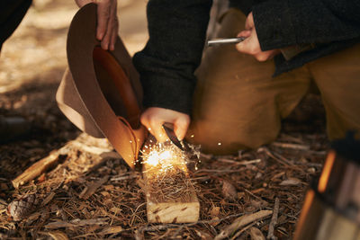 Midsection of bushcrafters enlighten fire in forest