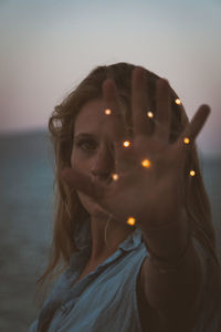 Portrait of woman holding illuminated lights against sky during sunset