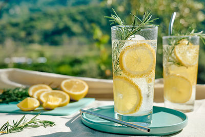 Summer refreshing lemonade drink or alcoholic cocktail with ice, rosemary and lemon slices on table