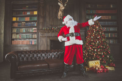 Man wearing santa claus costume standing by christmas tree at home