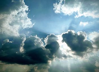 Low angle view of sunlight streaming through clouds