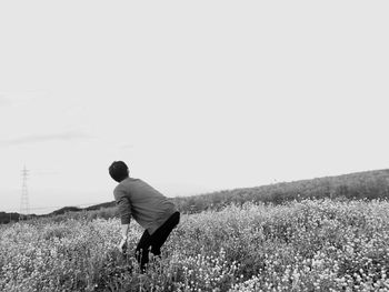 Man looking away while standing amidst flowering plants against sky