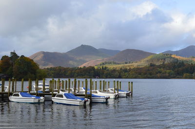 Boats moored in lake against cloudy sky